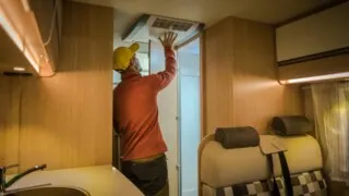 Photo of a man checking his RV rooftop air conditioner.