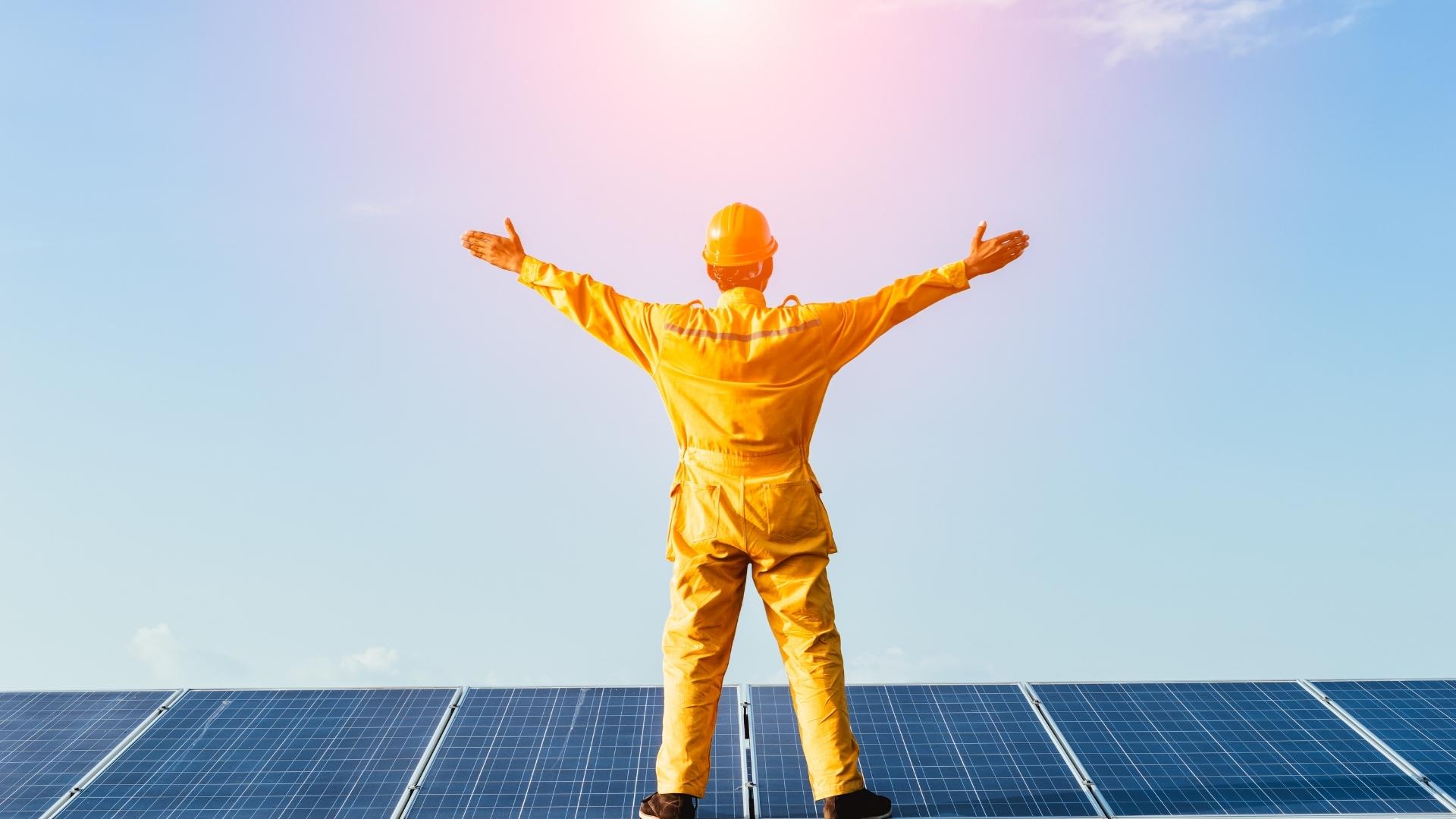 Photo of a solar technician standing on a solar panel array welcoming the power of the sun