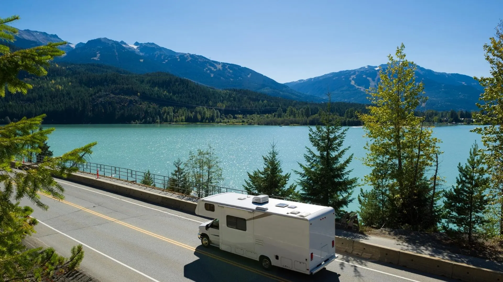 Photo of an RV driving along the road beside a lake