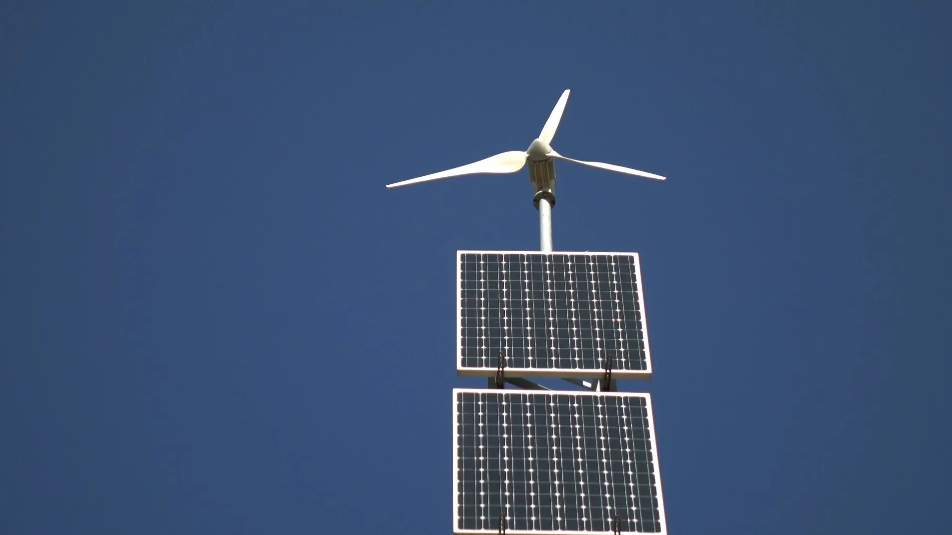 Photo of a wind turbine being used in conjunction with two solar panels