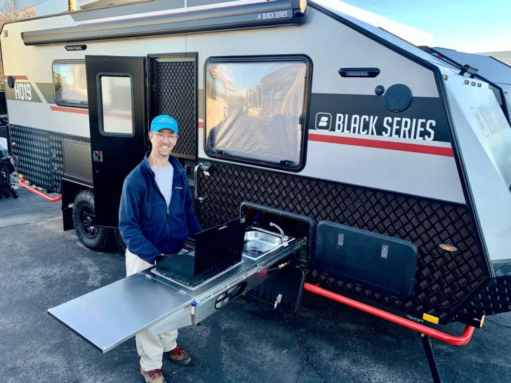 Photo of a Black Series travel trailer (HQ19) showing John at the outdoor kitchen.