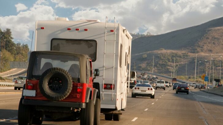 Photo of an RV towing a Jeep while traveling on the highway with traffic on all sides