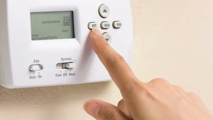 A woman setting the temperature on a thermostat