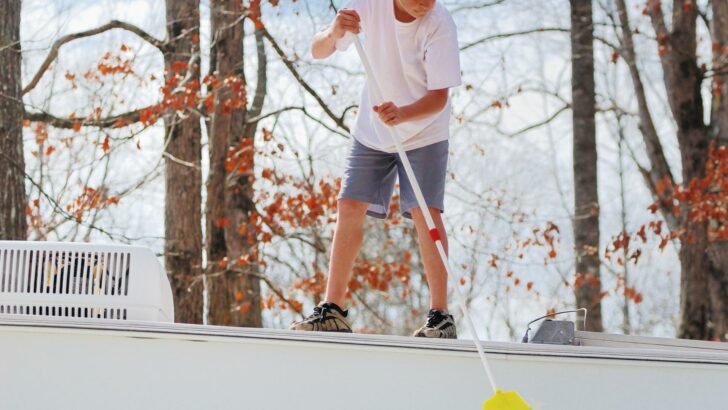Photo of a young man standing on an RV roof using a broom