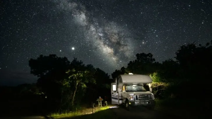 An RV parked in a field at night, with the starry sky above them