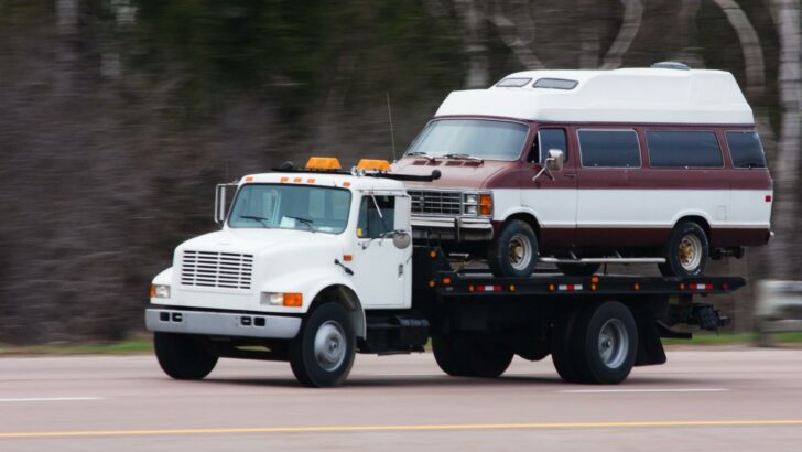 A flat bed truck carrying a vintage Class B camper van