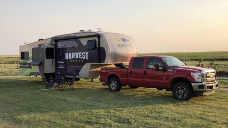 A Harvest Hosts 5th wheel parked in a field displaying the Harvest Hosts logo on the RV