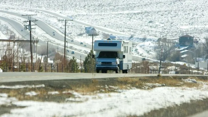 An RV traveling down the road in winter, with snow on the ground