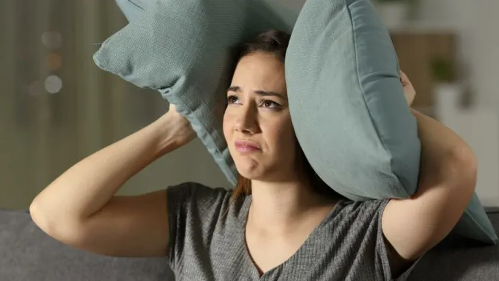 A woman holding a pillow over both ears to drown out noise
