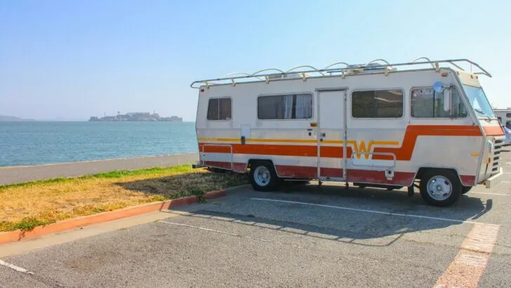An older RV parked in a rest area parking lot.