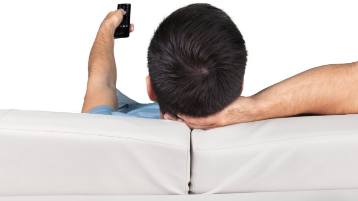 Un uomo sdraiato su un divano utilizza il telecomando della TV 