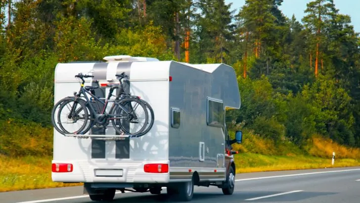 A Class C RV with a shelf/rack mounted high on the back of the rig carrying bikes