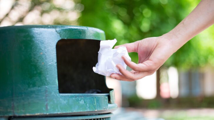 A woman's hand placing a wad of paper into a trash receptacle