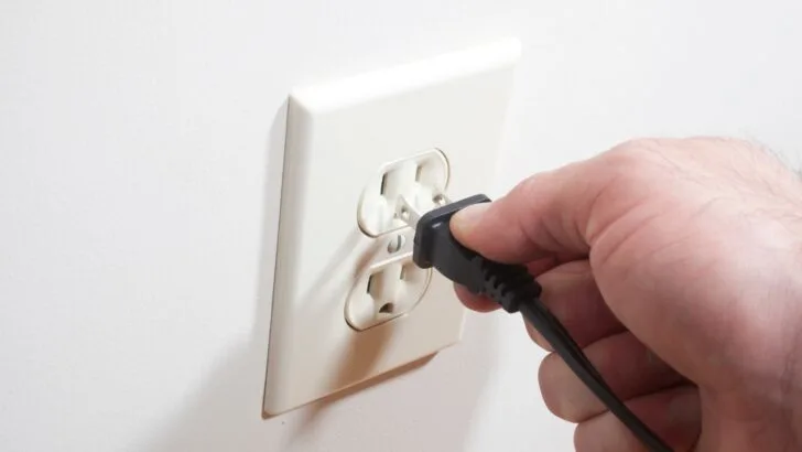 A person's hand plugging in a two-pronged 15-amp household plug