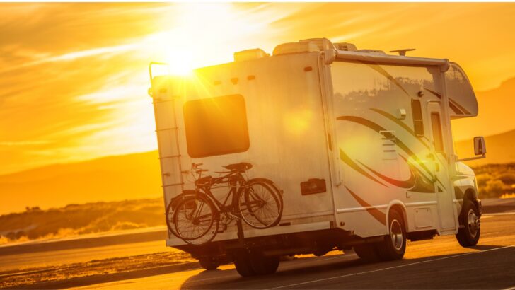 The back of an RV is shown with two bikes carried on a hitch rack and the ladder shown beside it