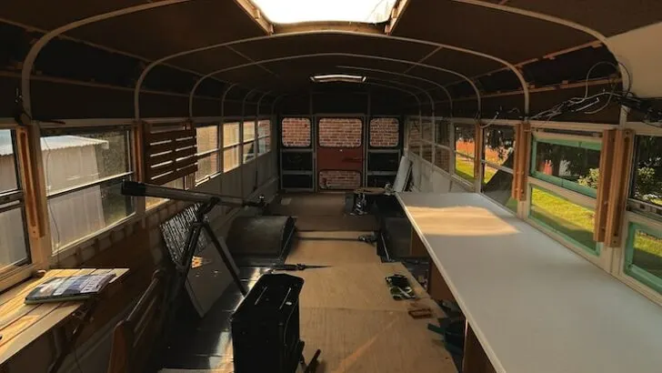 The interior of an old school bus with the seats removed and the skoolie conversion underway
