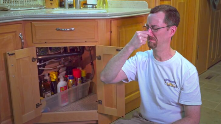 John beside the open cabinet under the kitchen sink, smelling the gray tank odor