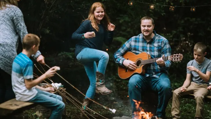 A family with children singing around a campfire