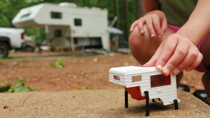 A child's toy illustrating the camper jacks on which a truck camper stands independently. Full size truck camper in the background.
