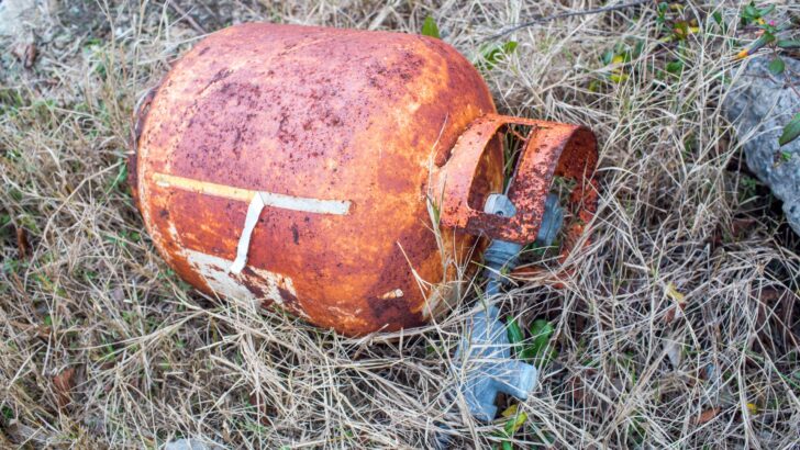 A rusty propane tank laying on the ground