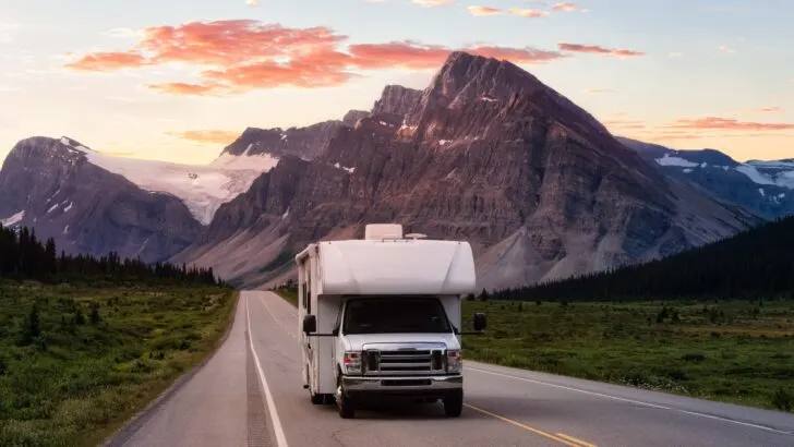 A Class C RV driving down the road with mountains in the background