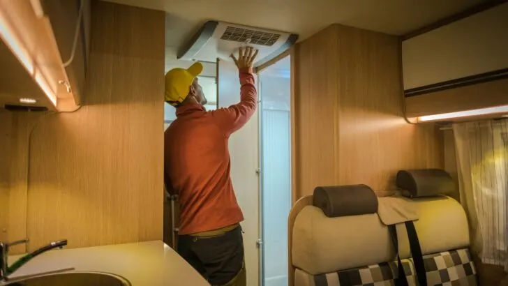 A man checking the air from an RV air conditioner in a small RV
