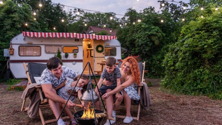 A family around a fire with their travel trailer in the background