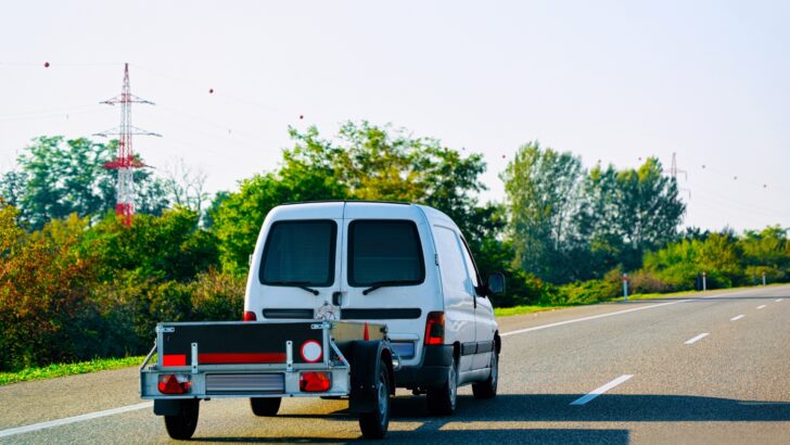 A small van towing a small, lightweight trailer