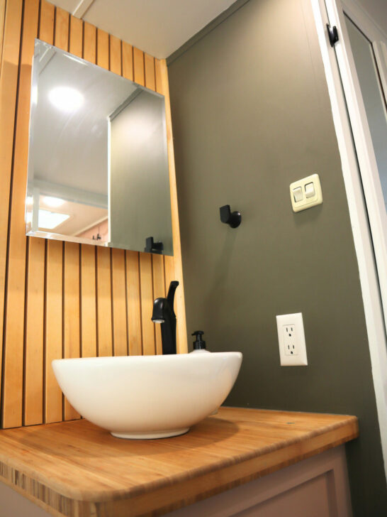 A stylish RV bathroom with vanity mirror storage and a vessel-style sink