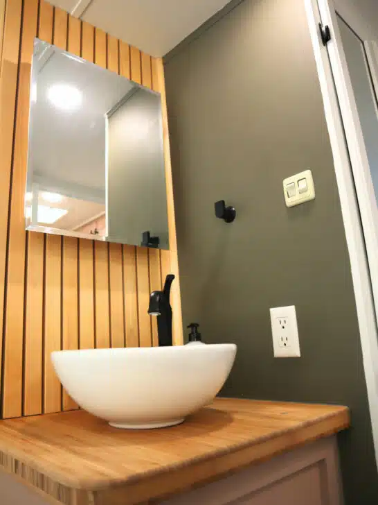 A stylish RV bathroom with vanity mirror storage and a vessel-style sink
