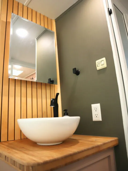 A stylish RV bathroom with vanity mirror storage and a vessel-style sink