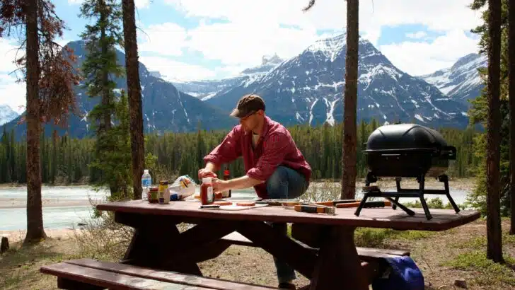 A man preparing food on a picnic table. Using a campground picnic table for unsanitary purposes might make people bad RV neighbors.